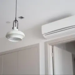 Biała klimatyzacja ścienna nad drzwiami, obok lampy wiszącej.