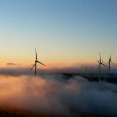 Wiatraki na wzgórzu, wyłaniające się z mgły o wschodzie słońca. Czysta energia, przyszłość bez opłat OZE.