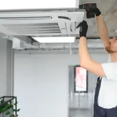 Technik w kasku montuje klimatyzator kasetonowy na suficie.