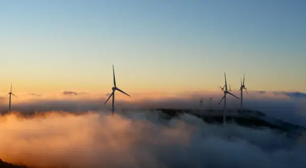 Wiatraki na wzgórzu, wyłaniające się z mgły o wschodzie słońca. Czysta energia, przyszłość bez opłat OZE.