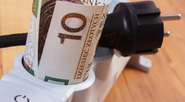 Zrolowany banknot 10 zł w gniazdku listwy zasilającej symbolizuje sposoby na oszczędzanie prądu i pieniędzy.