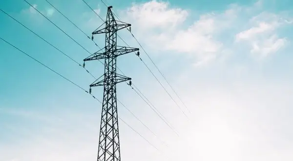 Wysoki słup energetyczny z przewodami, symbolizujący transport przesyłowy energii elektrycznej na tle błękitnego nieba z chmurami.