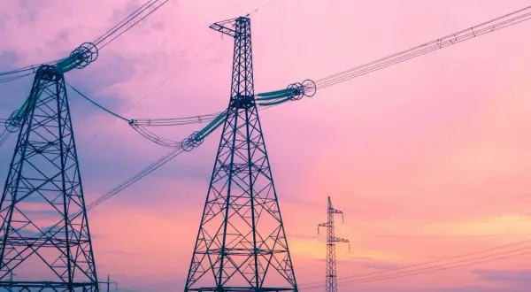 Wieże energetyczne na tle różowego nieba. Linie wysokiego napięcia, które niosą prąd o określonej częstotliwości, tworzą malowniczy krajobraz.