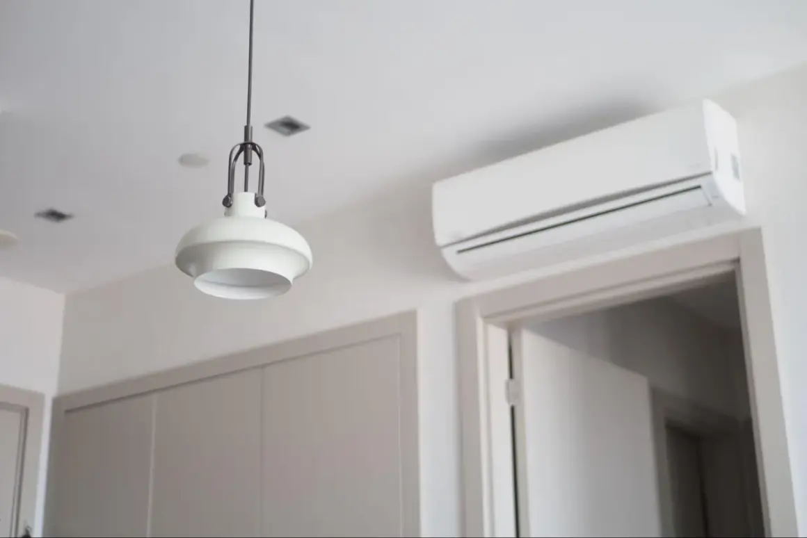 Biała klimatyzacja ścienna nad drzwiami, obok lampy wiszącej.