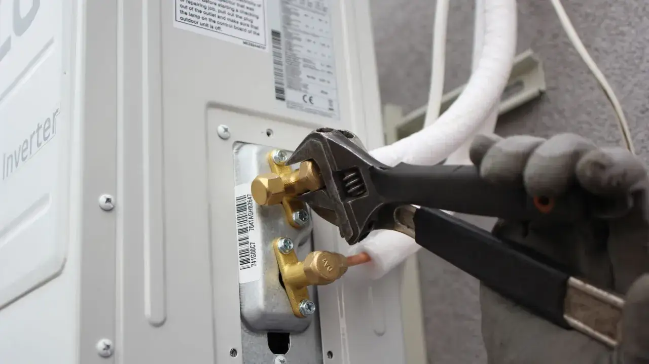 Instalator w rękawiczkach dokręca kluczem zawór jednostki klimatyzacyjnej.