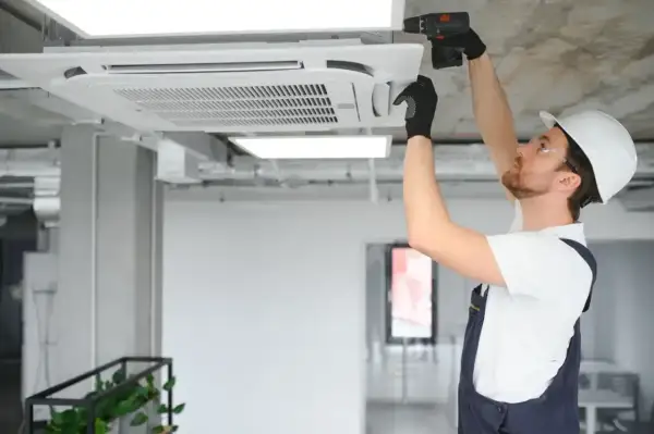 Technik w kasku montuje klimatyzator kasetonowy na suficie.